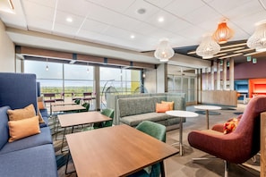 Un espacio lounge moderno con asientos, mesas y ventanas amplias que ofrecen una vista.
