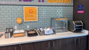 Een ontbijtbuffet met een bord waarop 'TOP IT BREAKFAST' staat en een bordje met de vraag 'DIEETBEPERKINGEN?' en een aantekening over eierenallergieën.