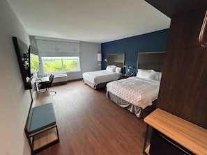 Habitación de hotel con dos camas, un escritorio y vistas al exterior.