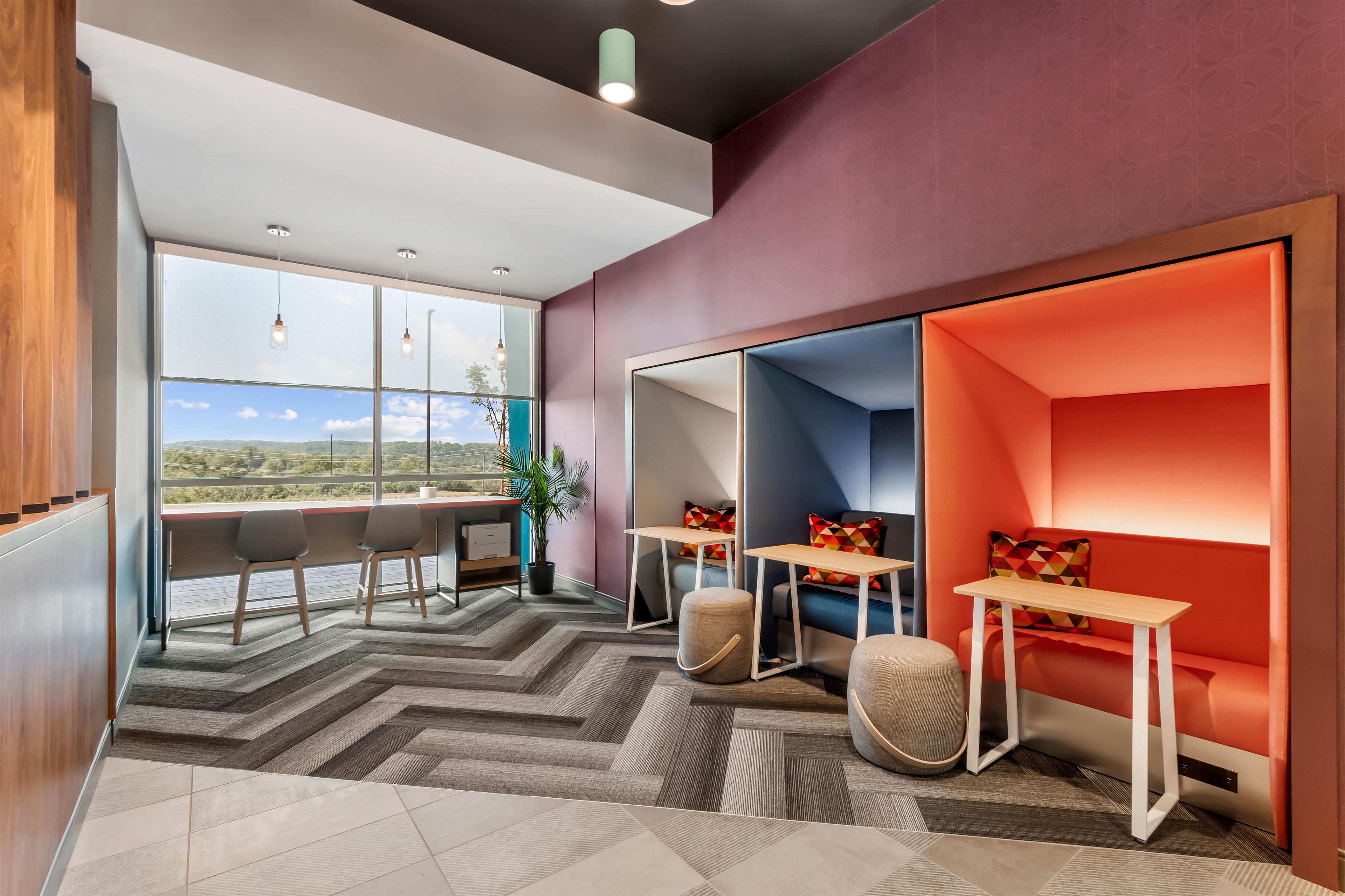A modern interior with a large window, a seating area with a red accent wall, and a herringbone-patterned floor.