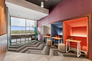 A modern interior with a large window, a seating area with a red accent wall, and a herringbone-patterned floor. - Tru By Hilton Bellefonte (Bellefonte)