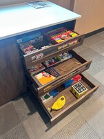 Un escritorio de madera con varios cajones que contienen diferentes juegos de mesa y una bolsa amarilla.