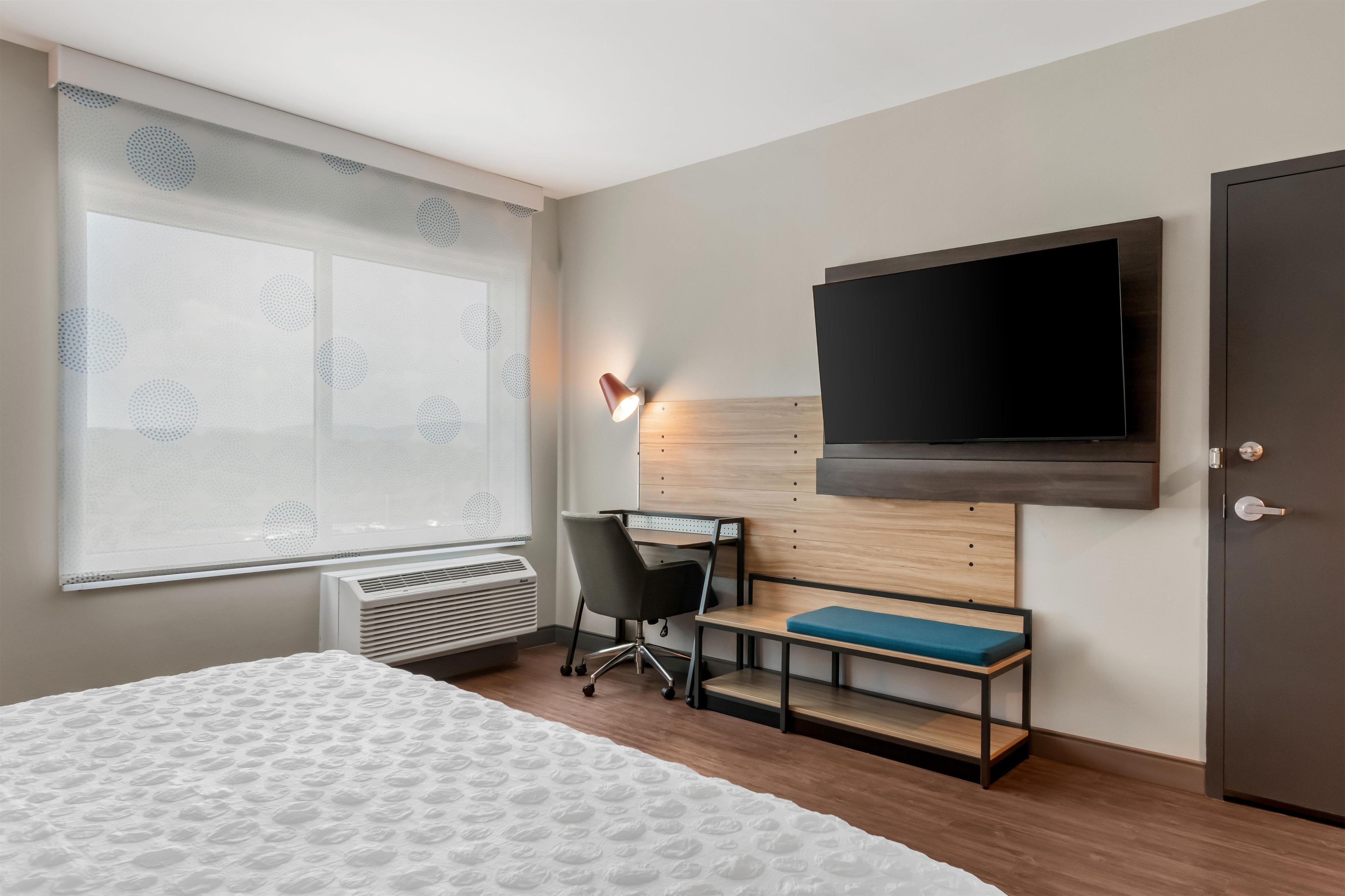 Habitación de hotel con cama, escritorio, silla, televisor y armario.