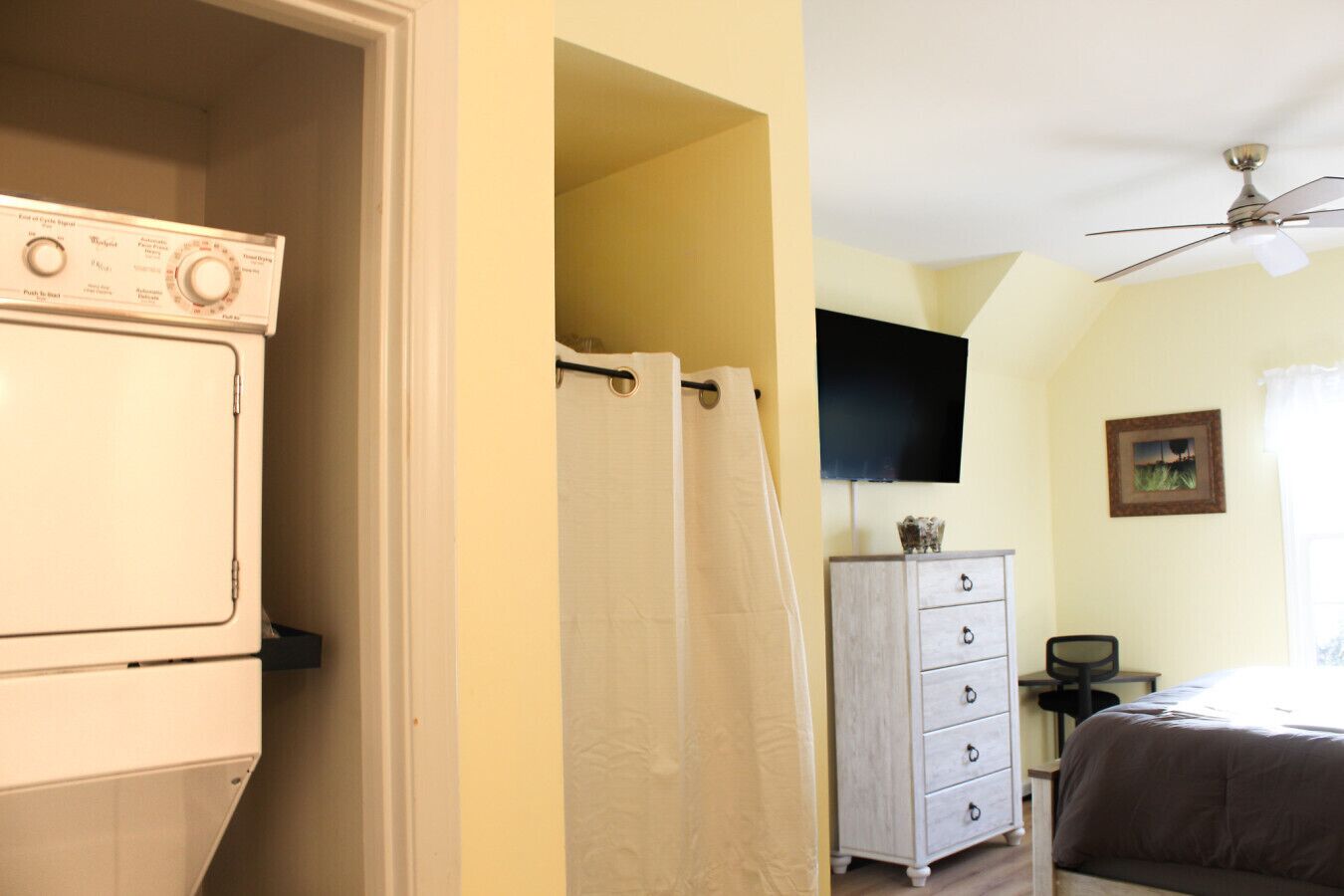 Une pièce équipée d’un lave-linge, d’un rideau de douche, d’une commode, d’un lit et d’un ventilateur de plafond.