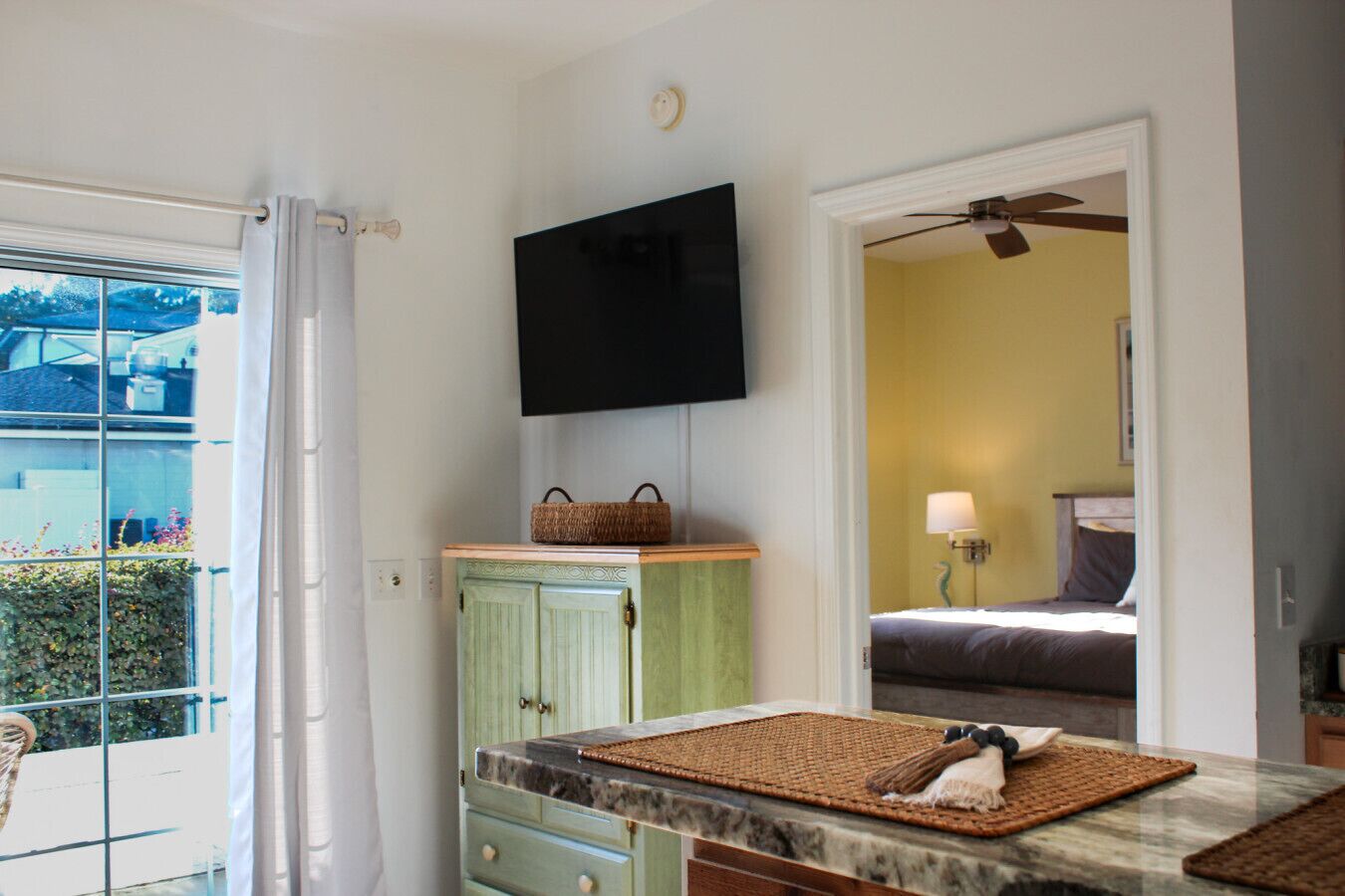 A compact room with a kitchenette, a bed, and a TV mounted on the wall.
