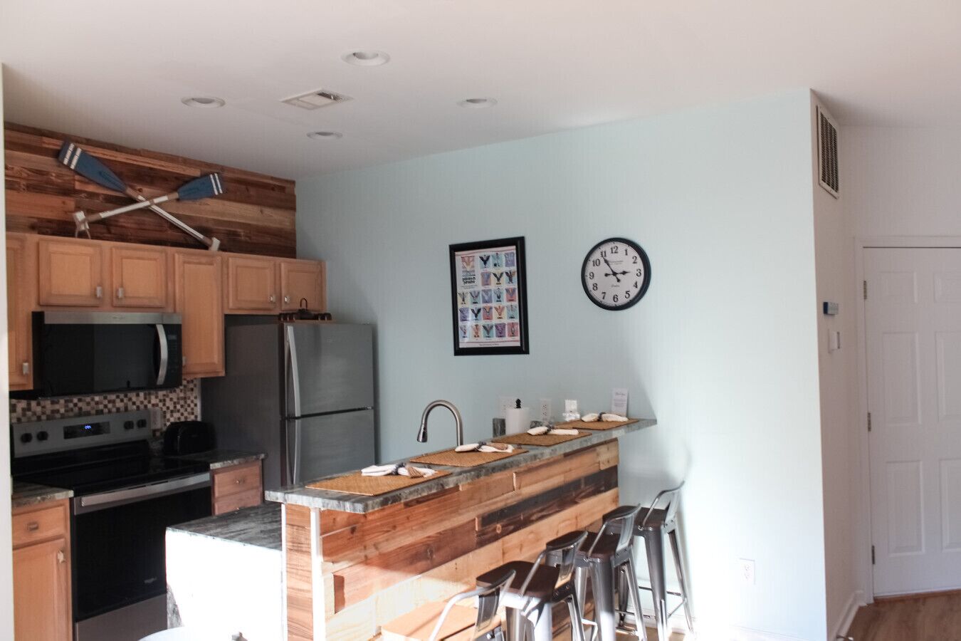 Una cocina con armarios de madera, un refrigerador de acero inoxidable, un microondas, una estufa y una isla de madera con taburetes.