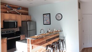 A kitchen with wooden cabinets, a stainless steel refrigerator, a microwave, a stove, and a wooden island with stools. - The Villa at 205 Royal Poste Rd (Sunset Beach)