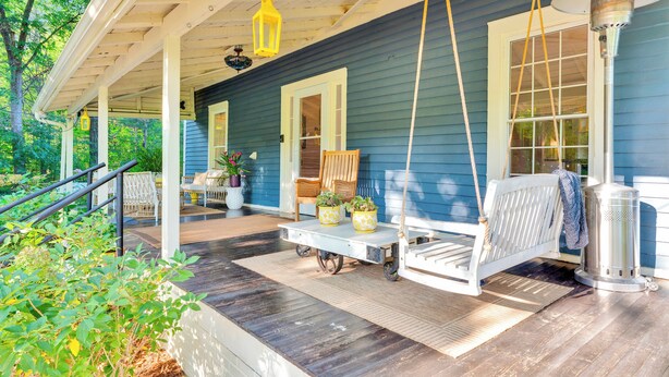 A covered porch with a swing chair, a table with potted plants, and a lantern. - Eclectic 1906 Farmhouse: 2 Acres, Fire Pit, Minutes to Lake Norman  & Charlotte (Huntersville)