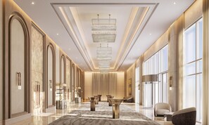 A spacious hotel lobby with a central chandelier, marble flooring, and a seating area with a sofa and armchairs.