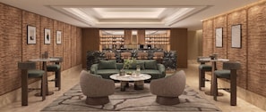 Een moderne zithoek met een groene bank, twee fauteuils, een marmeren bijzettafeltje en een kamerkleed met een patroon.