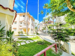 A residential area with a paved walkway, palm trees, and a building with a red-tiled roof. - BAVARO SEASIDE Villas BEACH HOTEL & SPA (Punta Cana)