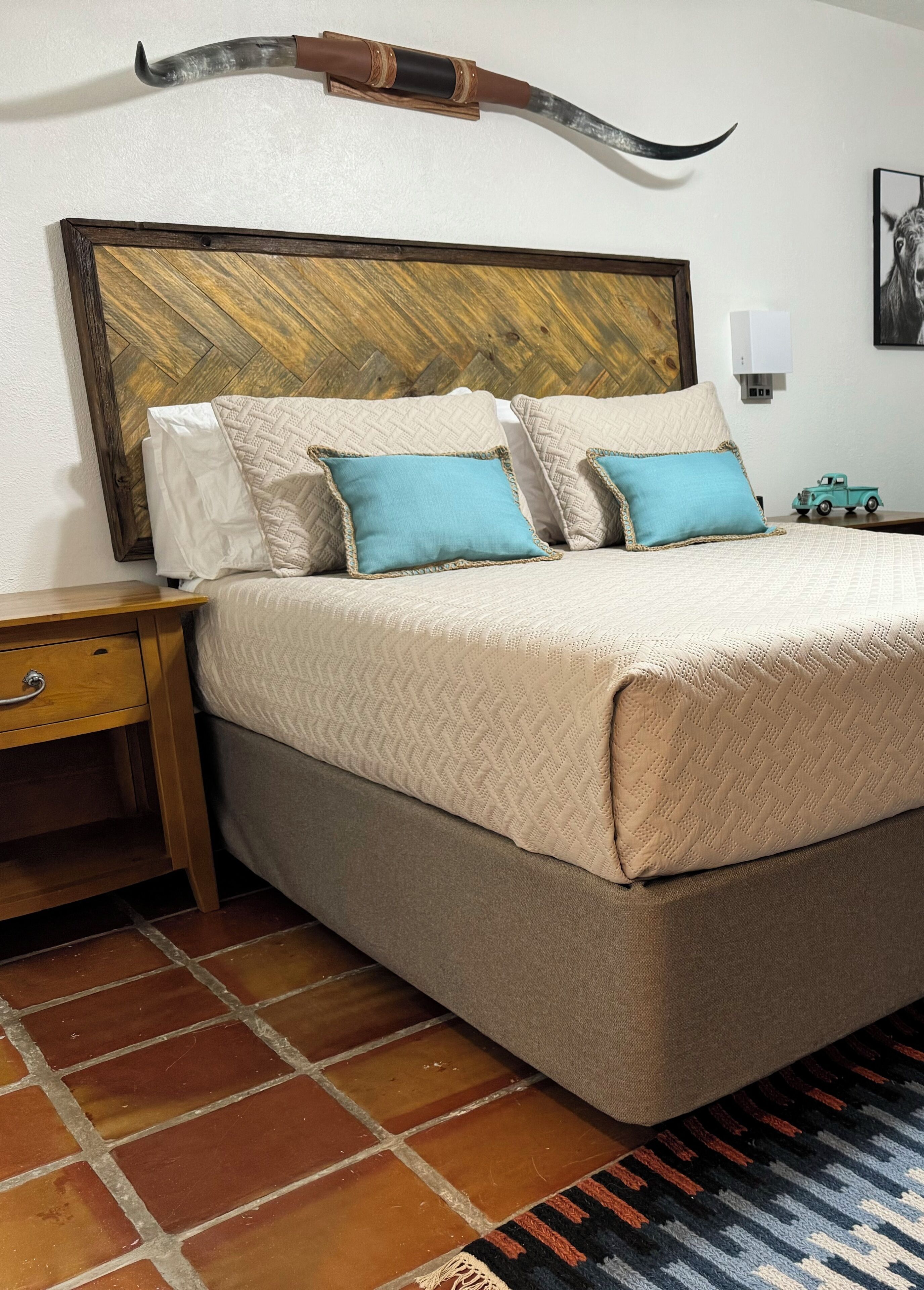 Quarto de hotel bem arrumado com uma cama grande, cabeceira de madeira, mesa de cabeceira e uma pequena mesa com um carrinho de brinquedo.