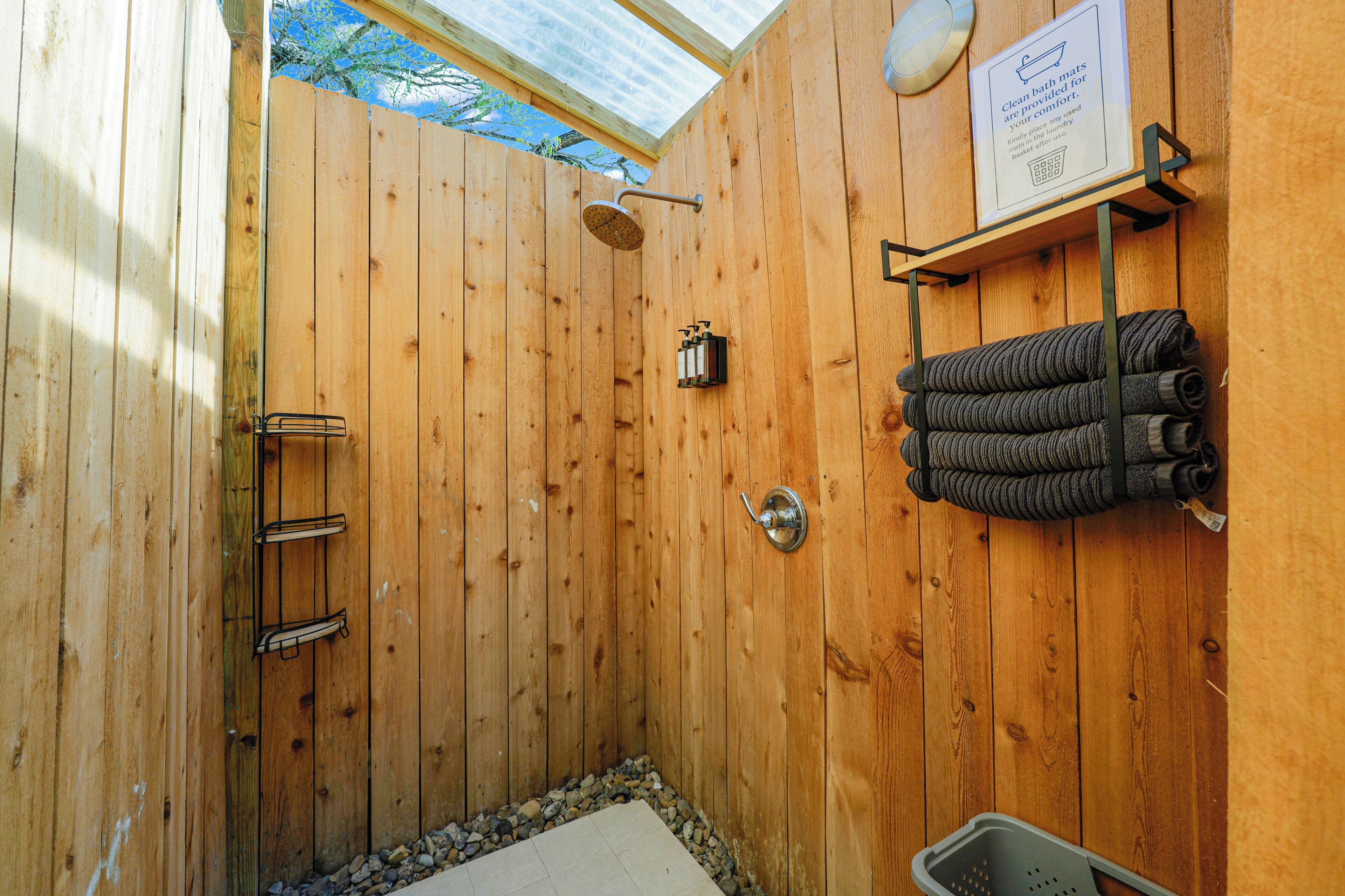 A wooden shower stall with a showerhead, a towel rack with towels, and a sign about bath mats.