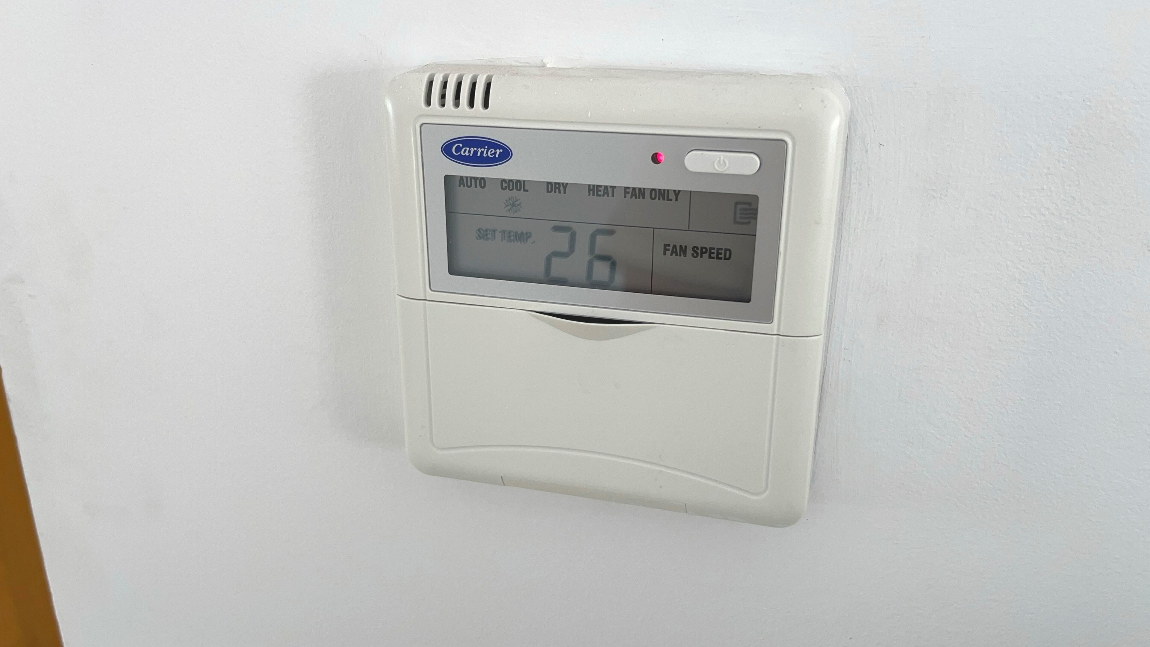 A wall-mounted thermostat with a digital display showing the temperature as 26 degrees.