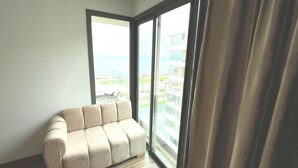 A room with a beige sofa, large windows, and a view of a building and greenery. - Modern sea view, near Hassan II Mosque, close to town center (Casablanca)