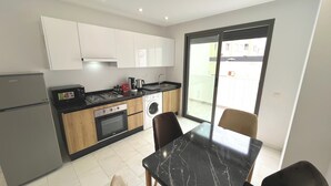 A modern kitchen with a refrigerator, stove, microwave, sink, and washing machine. There is a dining table with chairs and a sliding glass door leading to an outdoor area. - Modern sea view, near Hassan II Mosque, close to town center (Casablanca)