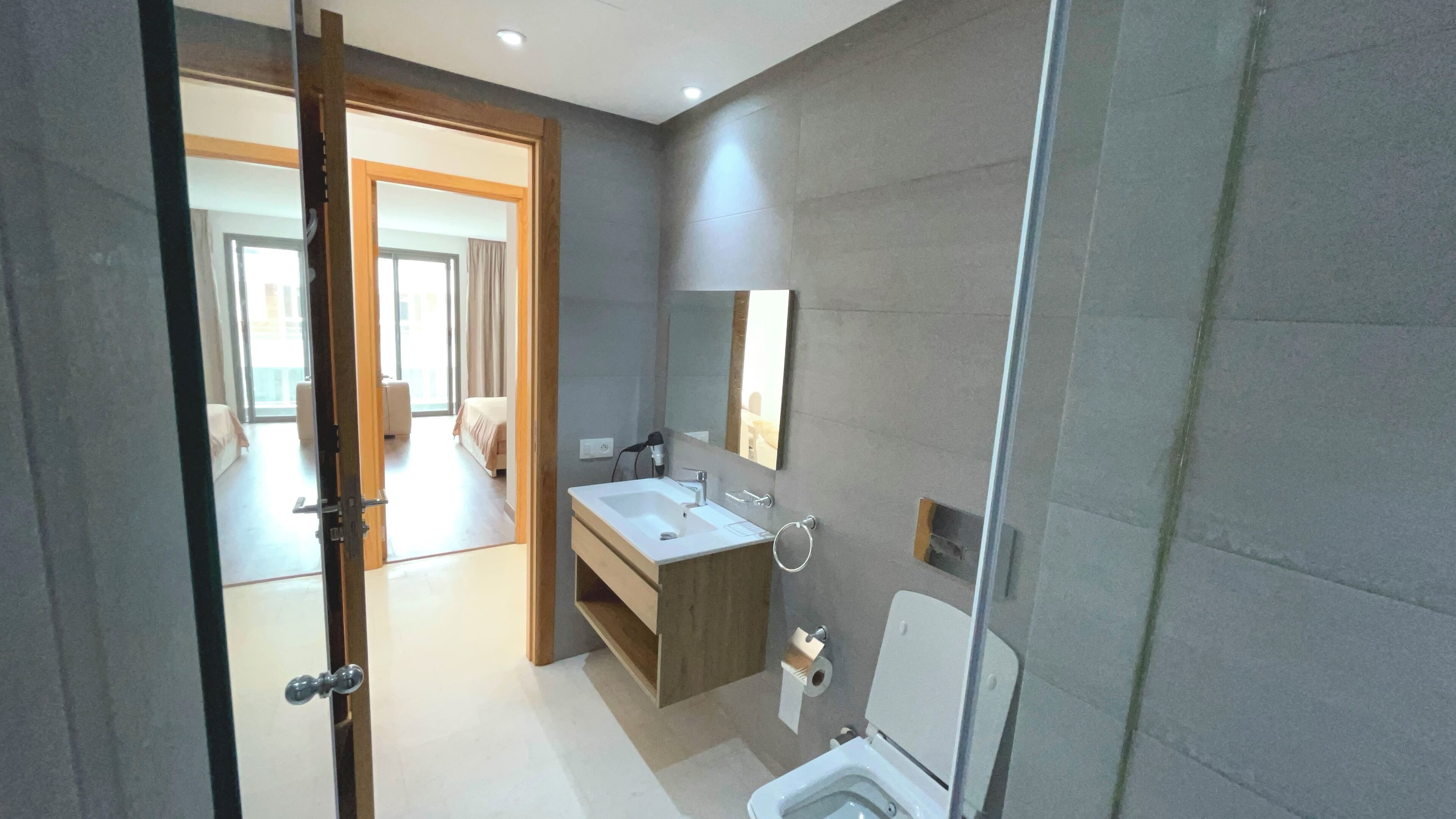 A modern bathroom with a sink, mirror, and toilet. There is a wooden vanity and a shower area visible.