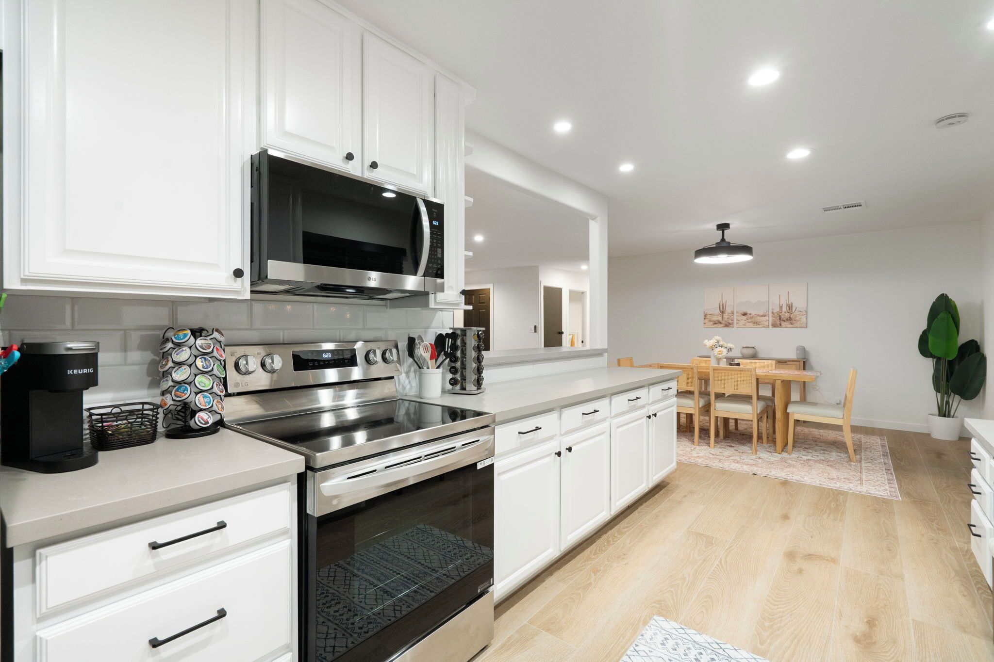 A modern kitchen with white cabinets, stainless steel appliances, and a dining area with a wooden table and chairs.