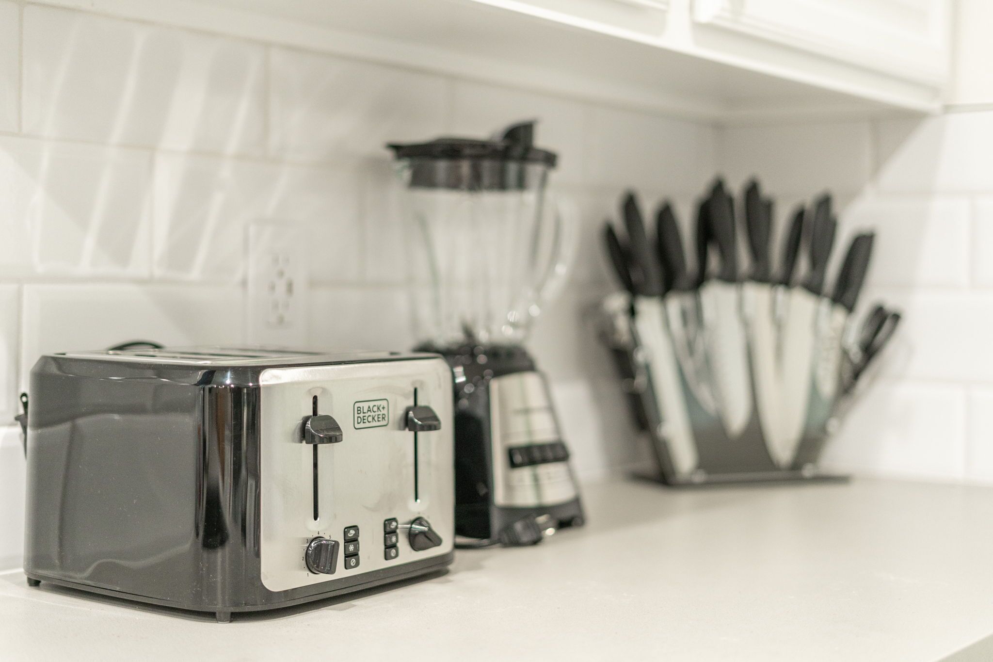 A kitchen with a toaster, a blender, and a knife block on the counter.