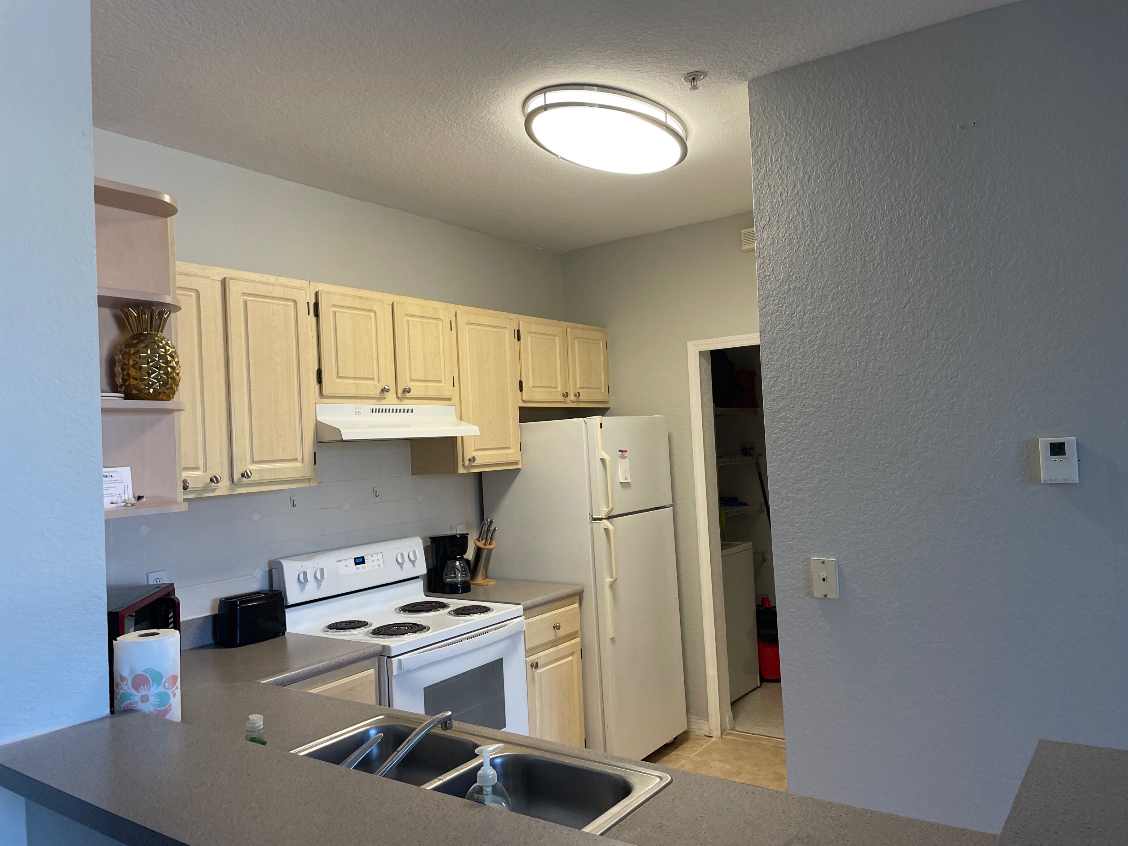 A compact kitchen with light wooden cabinets, a white stove, a refrigerator, and a built-in oven.