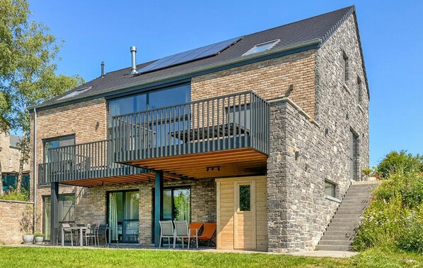 A modern two-story house with a stone facade, large windows, and a balcony with outdoor seating.