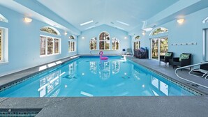 Una gran piscina interior con tragaluces, ventanas arqueadas y un flotador con forma de flamenco rosa.