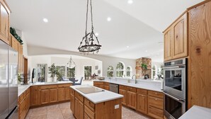 Una cocina amplia con armarios de madera, una isla central, electrodomésticos de acero inoxidable y una lámpara colgante.