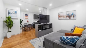 A modern living room with a grey sofa, a flat-screen TV, and a dining area with a table and chairs.