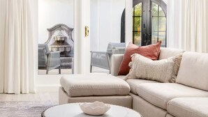 Una sala de estar moderna con un sofá seccional color beige, una mesa redonda de centro y vistas a un patio exterior con chimenea.