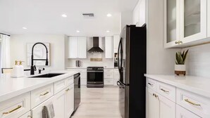Una cocina moderna con armarios blancos, electrodomésticos de acero inoxidable y tiradores dorados.