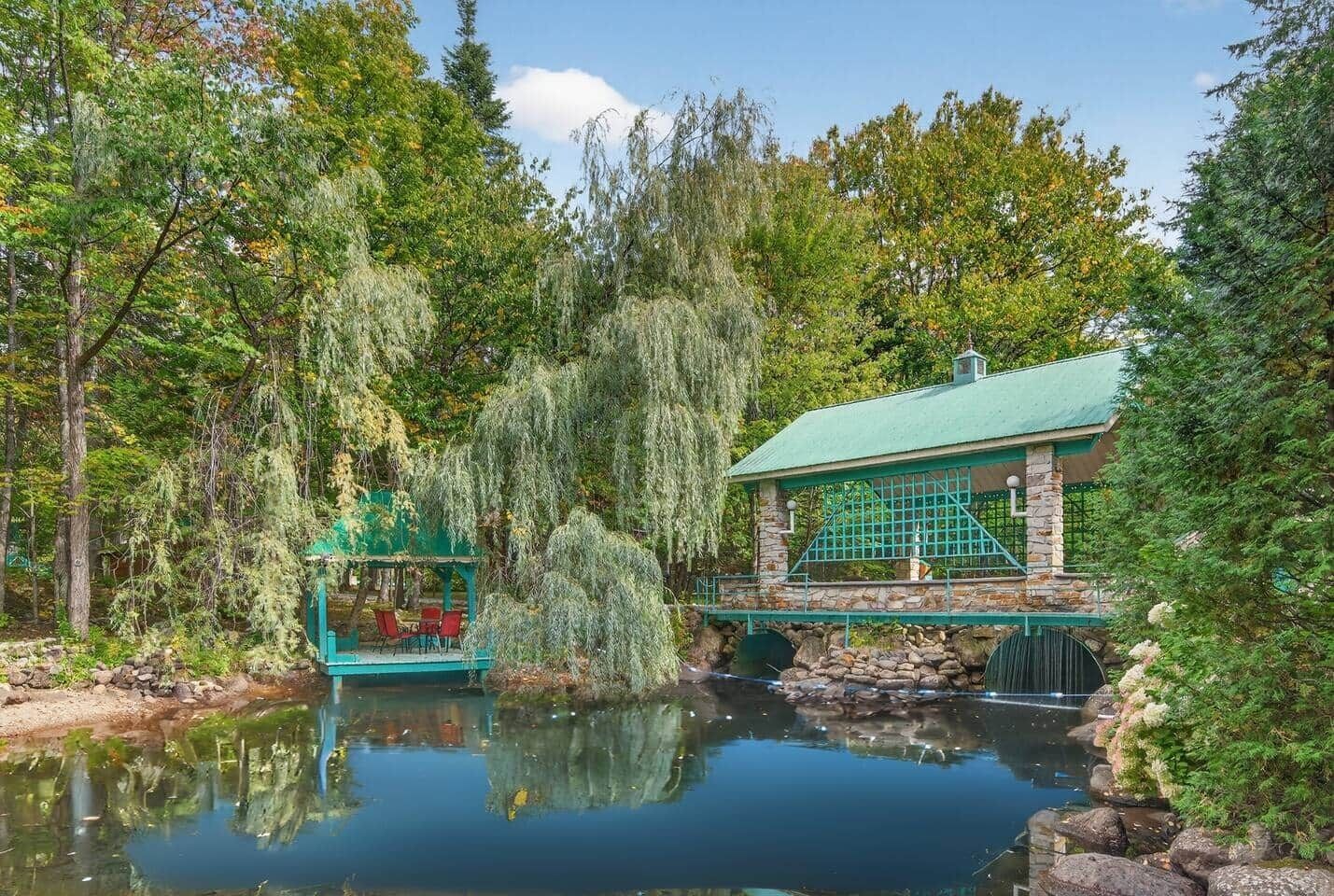Een rustige vijver met een prieel en een stenen gebouw met een groen dak.