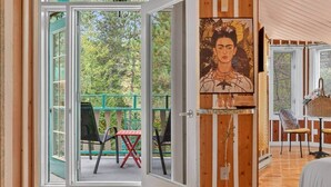 A room with a sliding glass door leading to an outdoor area with chairs and a table. There is a painting on the wall and a wicker basket on the table.