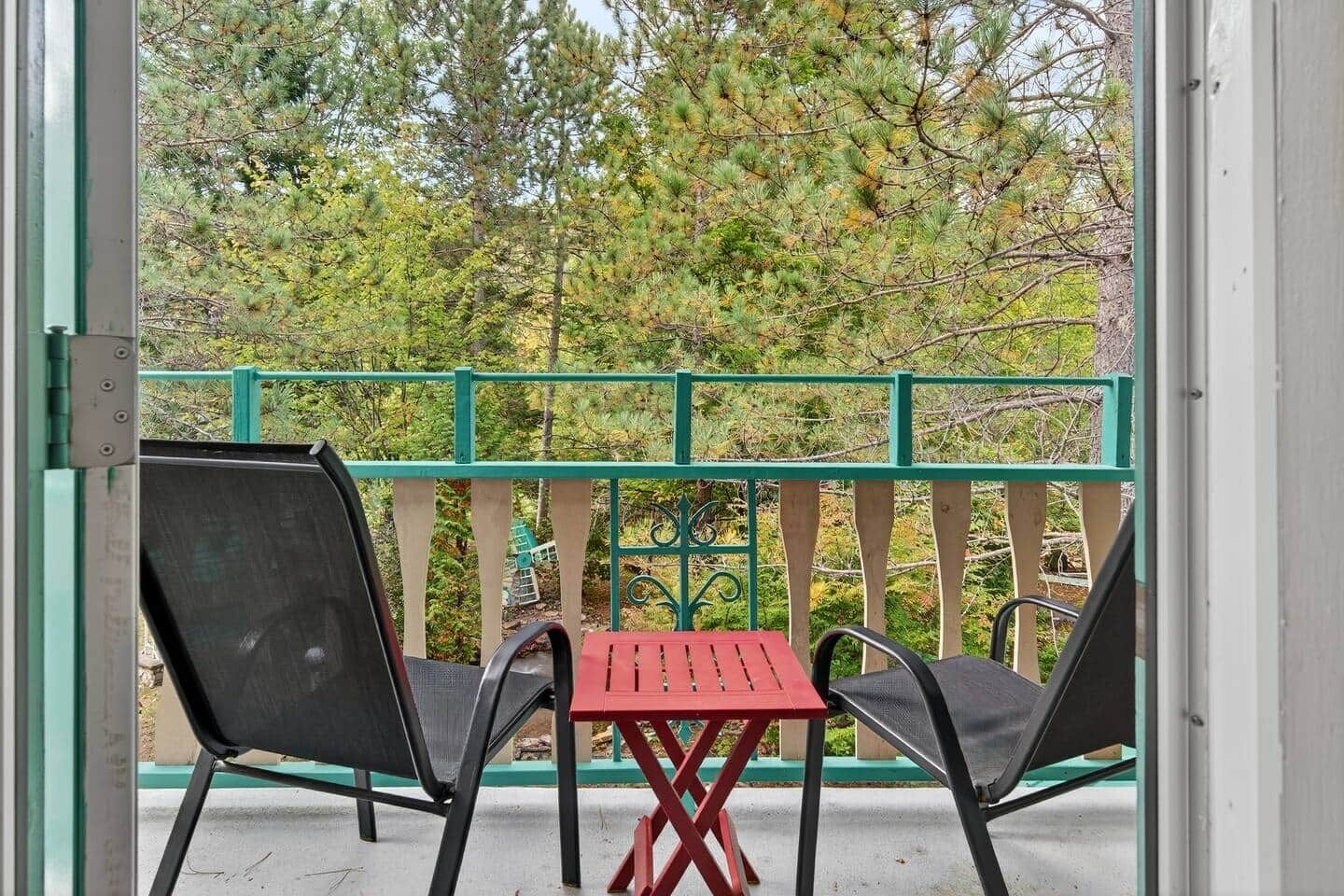 Un balcone con due sedie e un tavolino, vista su una zona boschiva.