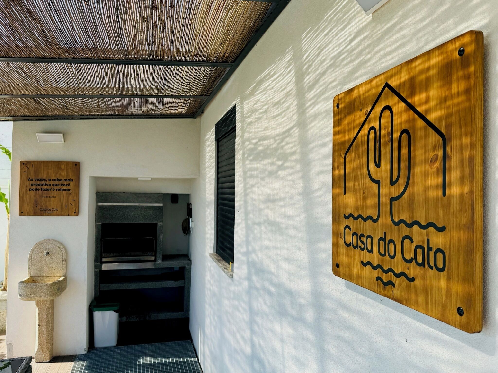 Ein Holzschild mit Kaktus-Design und dem Schriftzug "Casa do Cato" an einer weißen Wand.