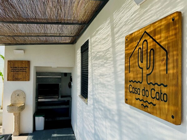 A wooden sign with a cactus design and the text "Casa do Cato" on a white wall.