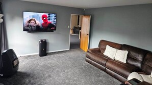 Un salon avec un canapé en cuir marron, un téléviseur à écran plat fixé au mur et un tapis gris.