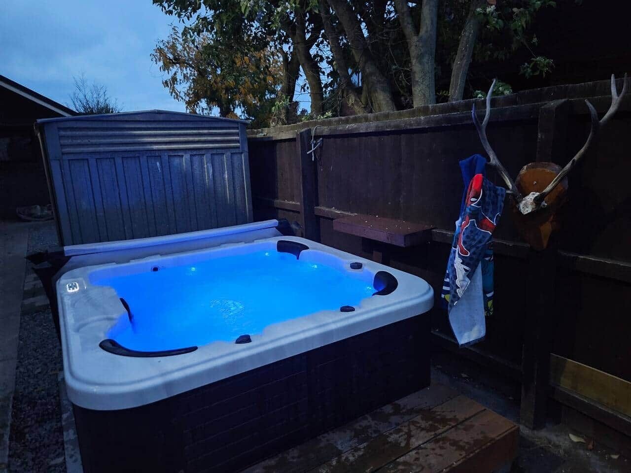 A hot tub with a blue light, a wooden deck, and a fence in the background.