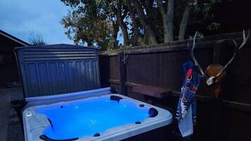 A hot tub with a blue light, a wooden deck, and a fence in the background.