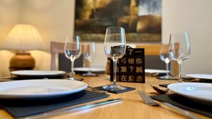 A dining table set with plates, cutlery, and wine glasses, with a menu stand in the center.