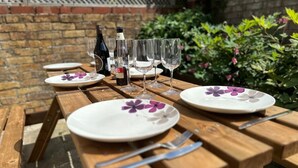 A wooden picnic table set outdoors with plates, cutlery, and wine bottles.