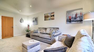 A living room with a sofa, ottoman, and a coffee table. There are wall art pieces and a lamp.