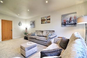 A living room with a sofa, ottoman, and a coffee table. There are wall art pieces and a lamp. - Hudson Apartment, Oakham Centre by Belmont Places (Rutland)