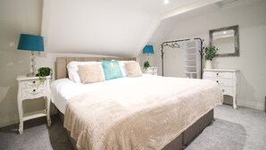 Ein Schlafzimmer mit einem großen Bett, zwei Nachttischen mit Lampen, einer Leiter, einem Spiegel und einer Pflanze.