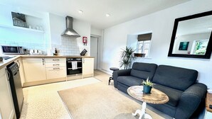 Eine moderne Küche mit Einbauofen und Mikrowelle, ein graues Sofa und ein kleiner runder Tisch mit einer Pflanze.