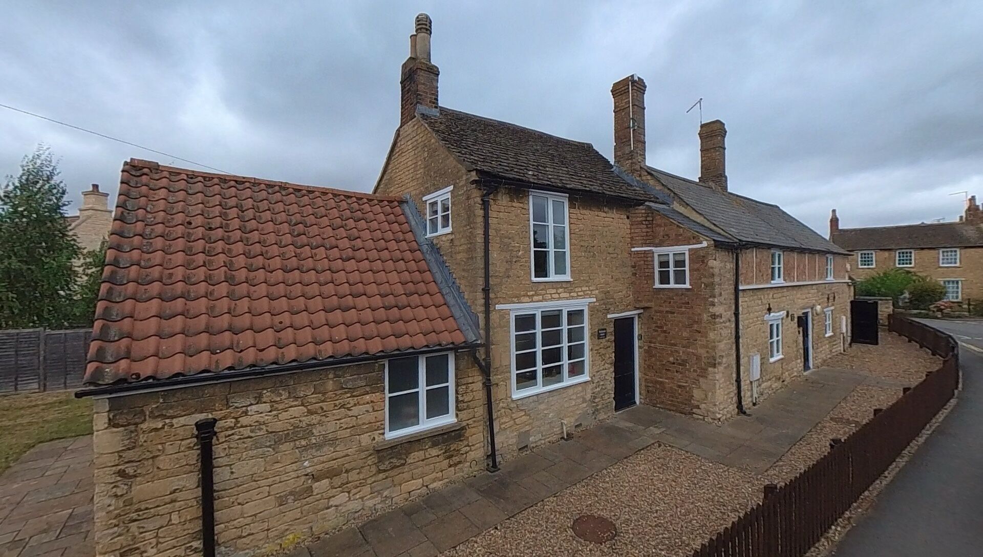 A traditional stone house with a tiled roof, a brick chimney, and a small front garden.