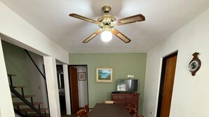A dining area with a long table, chairs, a ceiling fan, a painting, and a staircase. - Cabañas Sol Mediterraneo (Cosquín)
