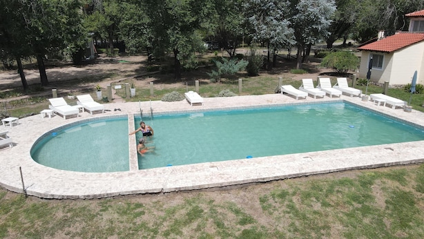 A rectangular swimming pool with a tiled edge, surrounded by white lounge chairs and a small deck area. - Cabañas Sol Mediterraneo (Cosquín)