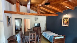 A room with a wooden ceiling, a bed with a striped bedspread, a table with chairs, a television, and a wall-mounted fan. - Cabañas Sol Mediterraneo (Cosquín)