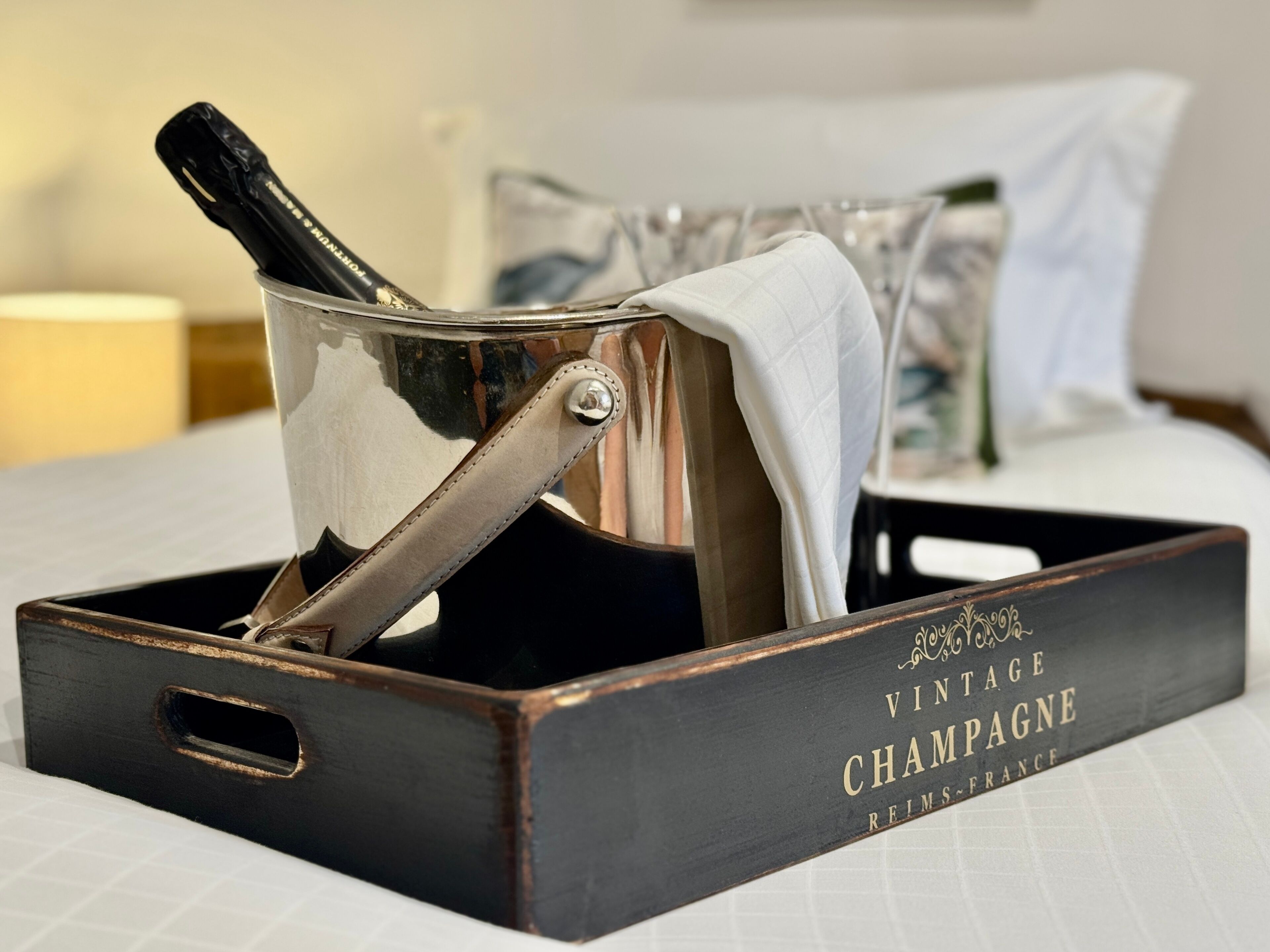 Een champagnefles uit een oudere jaargang in een metalen emmer met handvat, geplaatst op een houten dienblad met de tekst 