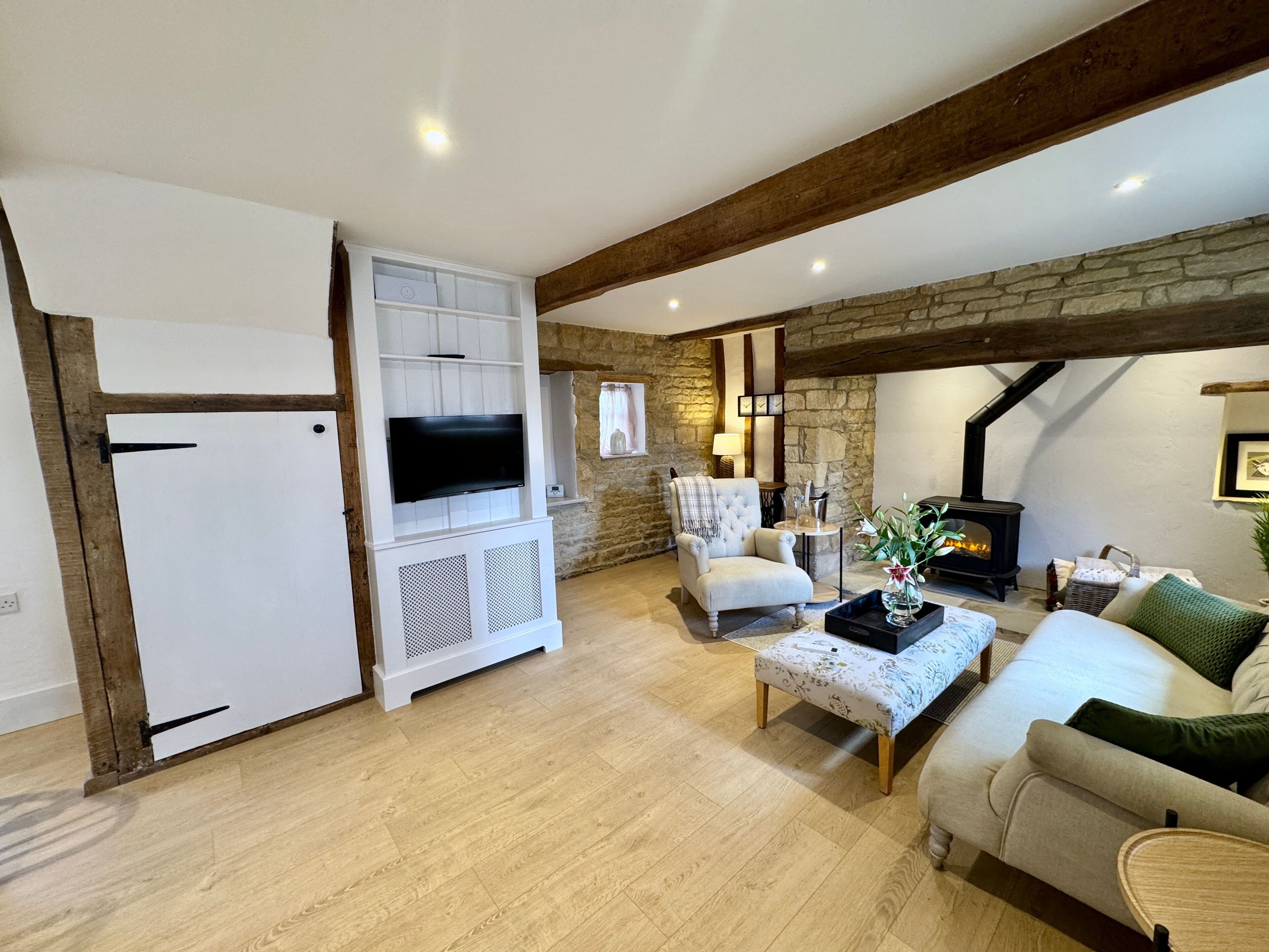 Una sala de estar acogedora con pared de piedra, chimenea, televisor, sofá confortable y un mueble blanco.